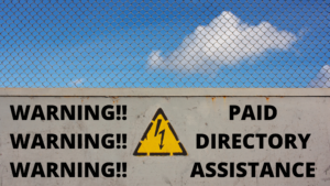 Blue sky with clouds and a brick wall with a caution sign that reads warning warning waning paid directory assistance.